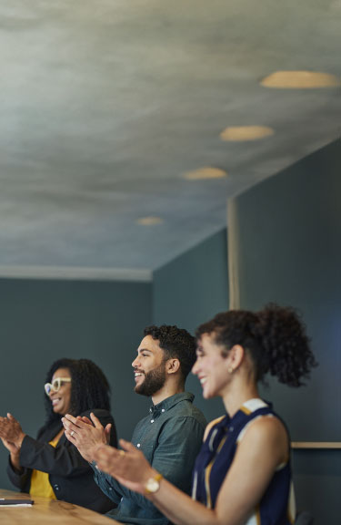 A group of people clapping in a meeting room to show appreciation and support.