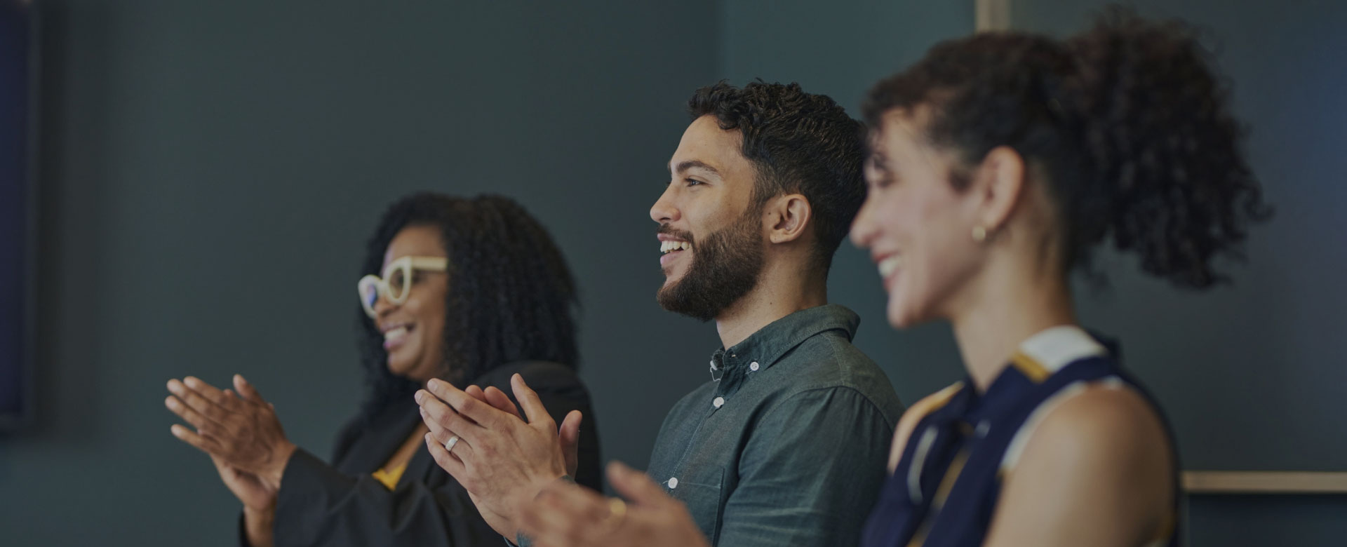 A group of people clapping in a meeting room to show appreciation and support.